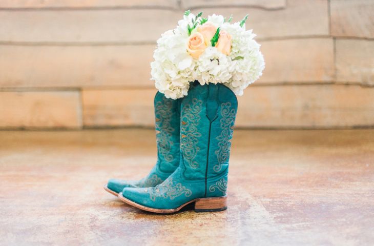 A turquoise pair of cowboy boots stuffed with white wedding flowers.