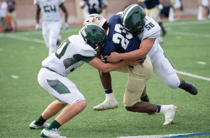 An action snapshot of football players tackling each other in a high school football game.